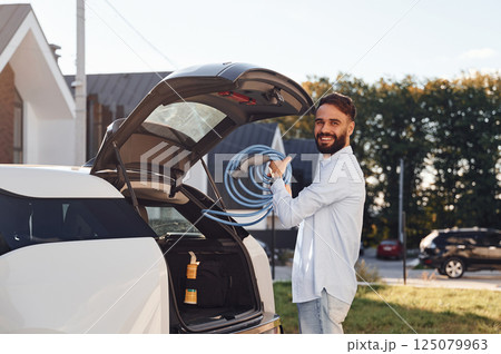 Taking charging wire from the truck. Young stylish man is with electric car at daytime 125079963