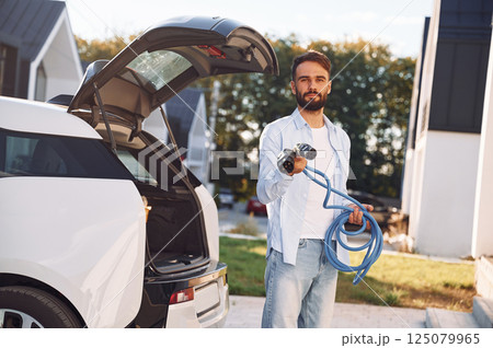 Holding yellow charging cable. Young stylish man is with electric car at daytime 125079965