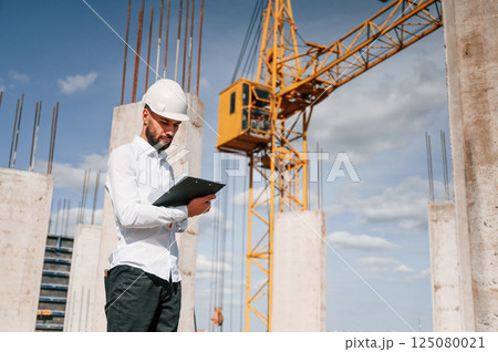 Inspector with notepad is standing on the construction site Inspector with notepad is standing on the construction site 125080021