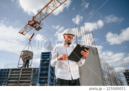 With notepad with documents. Foreman in uniform is working on the construction site With notepad with documents. Foreman in uniform is working on the construction site 125080051