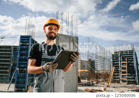 Control of the process. Foreman is with documents. Man in uniform is working on the construction site 125080086