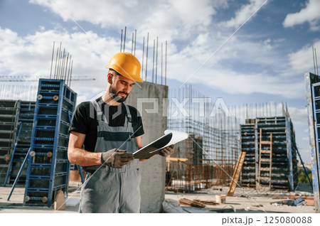 Control of the process. Foreman is with documents. Man in uniform is working on the construction site 125080088
