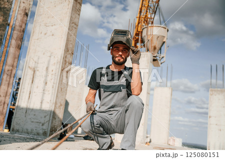 In welding mask. Man in uniform is working on the construction site In welding mask. Man in uniform is working on the construction site 125080151