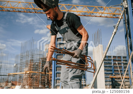 Working with rusty metal pieces. Man in uniform is on the construction site Working with rusty metal pieces. Man in uniform is on the construction site 125080156