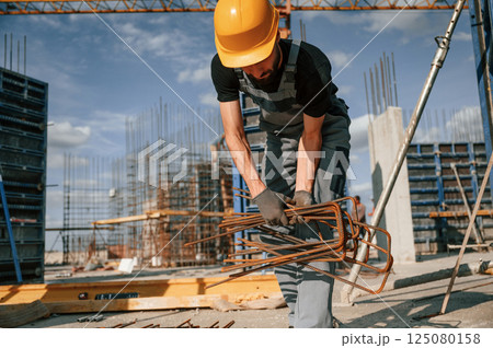 Working with rusty metal pieces. Man in uniform is on the construction site Working with rusty metal pieces. Man in uniform is on the construction site 125080158