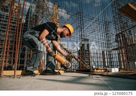 Using grinding machine to cut metal pieces. Man in uniform is working on the construction site 125080175