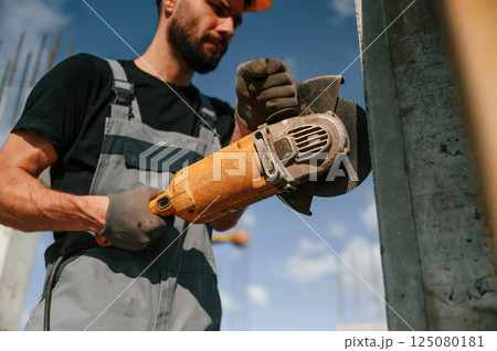 Holding grinding machine. Man in uniform is working on the construction site 125080181