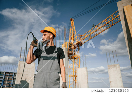 Portrait of man that is in uniform with the drill on the construction site Portrait of man that is in uniform with the drill on the construction site 125080196