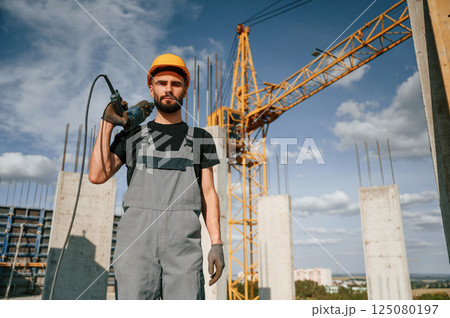 Portrait of man that is in uniform with the drill on the construction site Portrait of man that is in uniform with the drill on the construction site 125080197