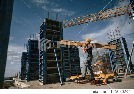 Yellow colored wooden plank. Man in uniform is working on the construction site 125080204
