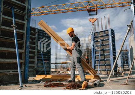Placing wooden plank on the floor. Man in uniform is working on the construction site 125080208