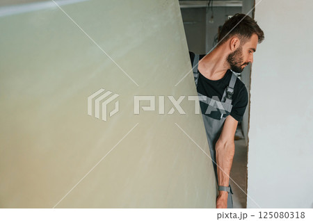 Moving big part of construction material by hands. The man is making repairs in the apartment 125080318
