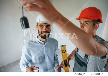 Working with light bulb. Two men is making repairs in the apartment together 125080346