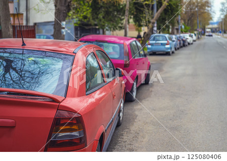 Row of cars parked on roadside. Colorful parked cars lined along urban street in day. Parked cars symbolize daily routine, urban lifestyle, city rhythm Row of cars parked on roadside. Colorful parked cars lined along urban street in day. Parked cars symbolize daily routine, urban lifestyle, city rhythm 125080406