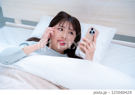 寝坊してスマホを見て焦る若い女性 寝坊してスマホを見て焦る若い女性 125080429