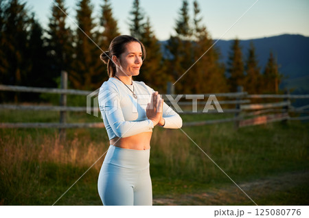 Woman practicing yoga and meditating outdoors in the mountains in a serene, natural setting. Female performing yoga pose, with backdrop of beautiful mountain landscape at sunrise or sunset. Woman practicing yoga and meditating outdoors in the mountains in a serene, natural setting. Female performing yoga pose, with backdrop of beautiful mountain landscape at sunrise or sunset. 125080776