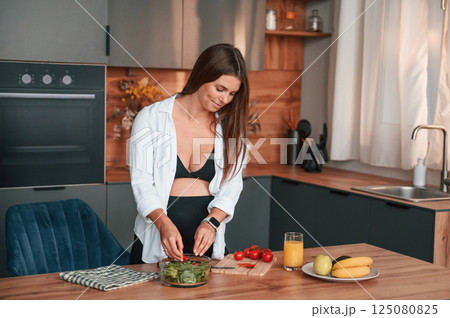 Preparing the salad on kitchen. Beautiful pregnant woman is indoors at home 125080825