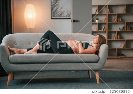 Laying down on the sofa. Beautiful pregnant woman is indoors at home 125080856