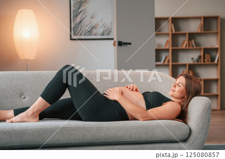 Laying down on the sofa. Beautiful pregnant woman is indoors at home 125080857