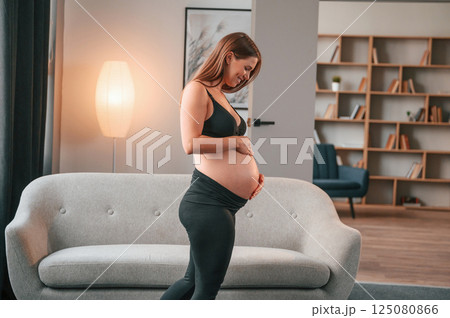 Standing in the domestic room and touching the belly. Beautiful pregnant woman is indoors at home Standing in the domestic room and touching the belly. Beautiful pregnant woman is indoors at home 125080866