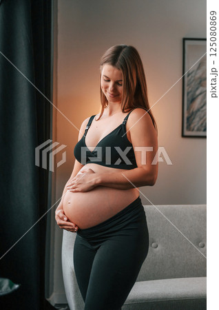 Standing in the domestic room and touching the belly. Beautiful pregnant woman is indoors at home Standing in the domestic room and touching the belly. Beautiful pregnant woman is indoors at home 125080869