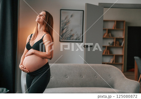 Standing and having positive mood. Beautiful pregnant woman is indoors at home 125080872