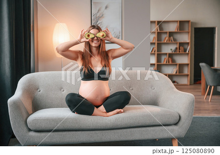 Holding avocado. Beautiful pregnant woman is indoors at home Holding avocado. Beautiful pregnant woman is indoors at home 125080890