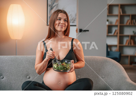 With salad. Conception of healthy eating. Beautiful pregnant woman is indoors at home With salad. Conception of healthy eating. Beautiful pregnant woman is indoors at home 125080902