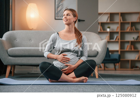 Sitting on the yoga mat. Beautiful pregnant woman is indoors at home 125080912