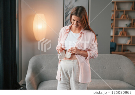 Holding cute little socks. Beautiful pregnant woman is indoors at home 125080965