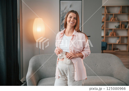 Holding cute little socks. Beautiful pregnant woman is indoors at home Holding cute little socks. Beautiful pregnant woman is indoors at home 125080966