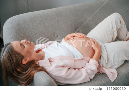 Resting on the sofa. Beautiful pregnant woman is indoors at home Resting on the sofa. Beautiful pregnant woman is indoors at home 125080980