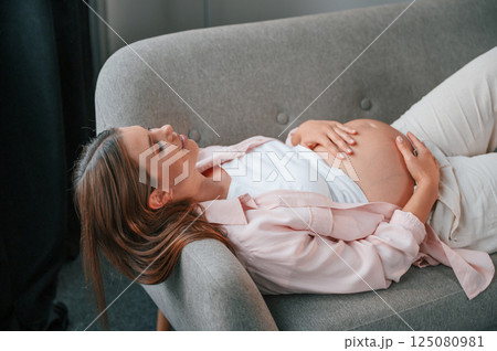 Resting on the sofa. Beautiful pregnant woman is indoors at home Resting on the sofa. Beautiful pregnant woman is indoors at home 125080981