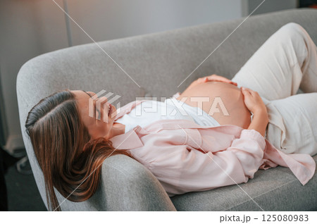 Resting on the sofa. Beautiful pregnant woman is indoors at home Resting on the sofa. Beautiful pregnant woman is indoors at home 125080983