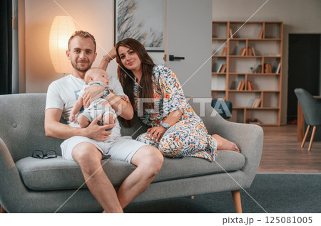 Sitting on the sofa. Happy couple with their newborn boy is at home together 125081005
