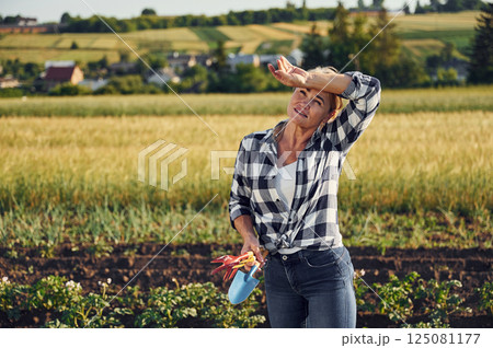 Standing and holding little showel and other garden tools. Woman is on the agricultural field at daytime Standing and holding little showel and other garden tools. Woman is on the agricultural field at daytime 125081177
