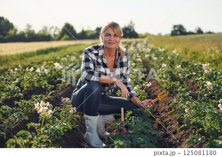 Sitting and working by using garden tools. Woman is on the agricultural field at daytime Sitting and working by using garden tools. Woman is on the agricultural field at daytime 125081180