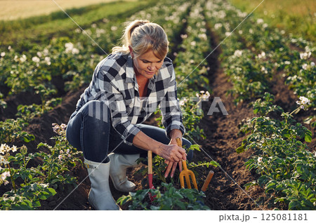 Sitting and working by using garden tools. Woman is on the agricultural field at daytime Sitting and working by using garden tools. Woman is on the agricultural field at daytime 125081181