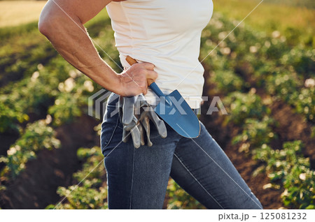 Close up view. With gloves and little showel. Woman is on the agricultural field at daytime Close up view. With gloves and little showel. Woman is on the agricultural field at daytime 125081232