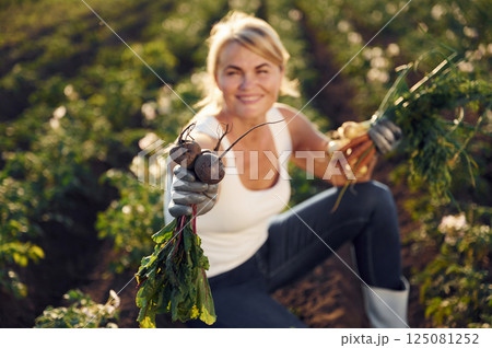 Onions, beetroots and carrots is in the hands. Woman is on the agricultural field at daytime Onions, beetroots and carrots is in the hands. Woman is on the agricultural field at daytime 125081252