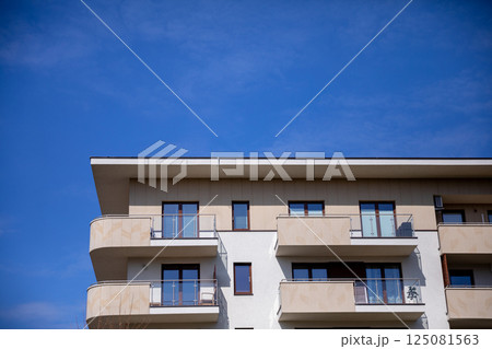 A sleek and modern apartment building stands elegantly against a clear and beautiful blue sky above A sleek and modern apartment building stands elegantly against a clear and beautiful blue sky above 125081563
