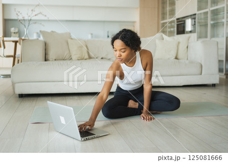 Yoga fitness workout training online. African woman practicing yoga with online lessons in laptop at home. Girl doing sports exercise on yoga mat. Woman have workout for weight loss. Sport fitness Yoga fitness workout training online. African woman practicing yoga with online lessons in laptop at home. Girl doing sports exercise on yoga mat. Woman have workout for weight loss. Sport fitness 125081666