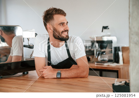 Beautiful portrait. Cafe worker in white shirt and black apron is indoors Beautiful portrait. Cafe worker in white shirt and black apron is indoors 125081954