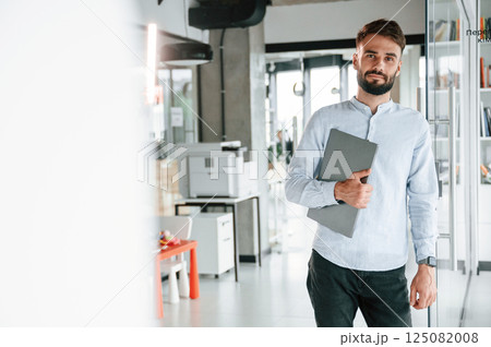 With laptop in hand. Young office worker in formal clothes is indoors 125082008