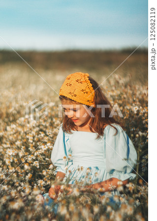 Smiling girl in blue linen dress and natural yellow knitted handmade kerchief in daisy field in summer day 125082119