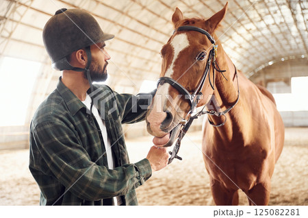 Taking care of animal. Young man with a horse is in the hangar Taking care of animal. Young man with a horse is in the hangar 125082281