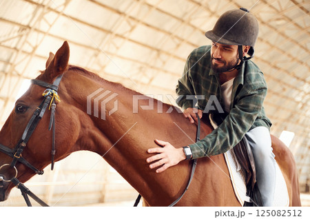 Jockey is in the saddle. Young man with a horse is in the hangar 125082512
