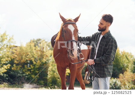 In casual clothes. Young man with a horse is outdoors In casual clothes. Young man with a horse is outdoors 125082525