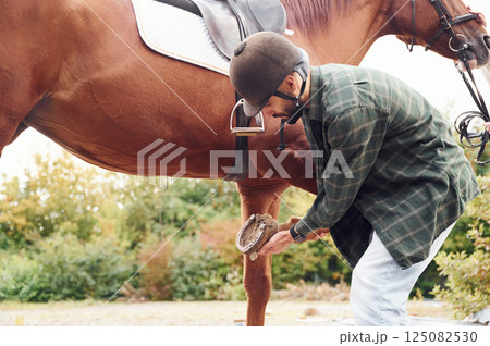 Setting up equipment for the ride. Young man with a horse is outdoors 125082530