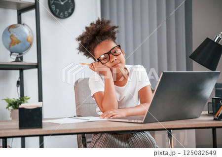 With pen. Cute female african american student child is sitting by the laptop 125082649